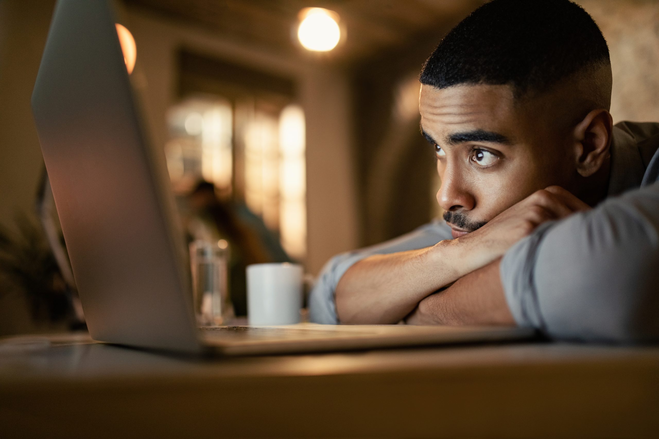 Young black businessman leaning on his desk while working on a computer at night.